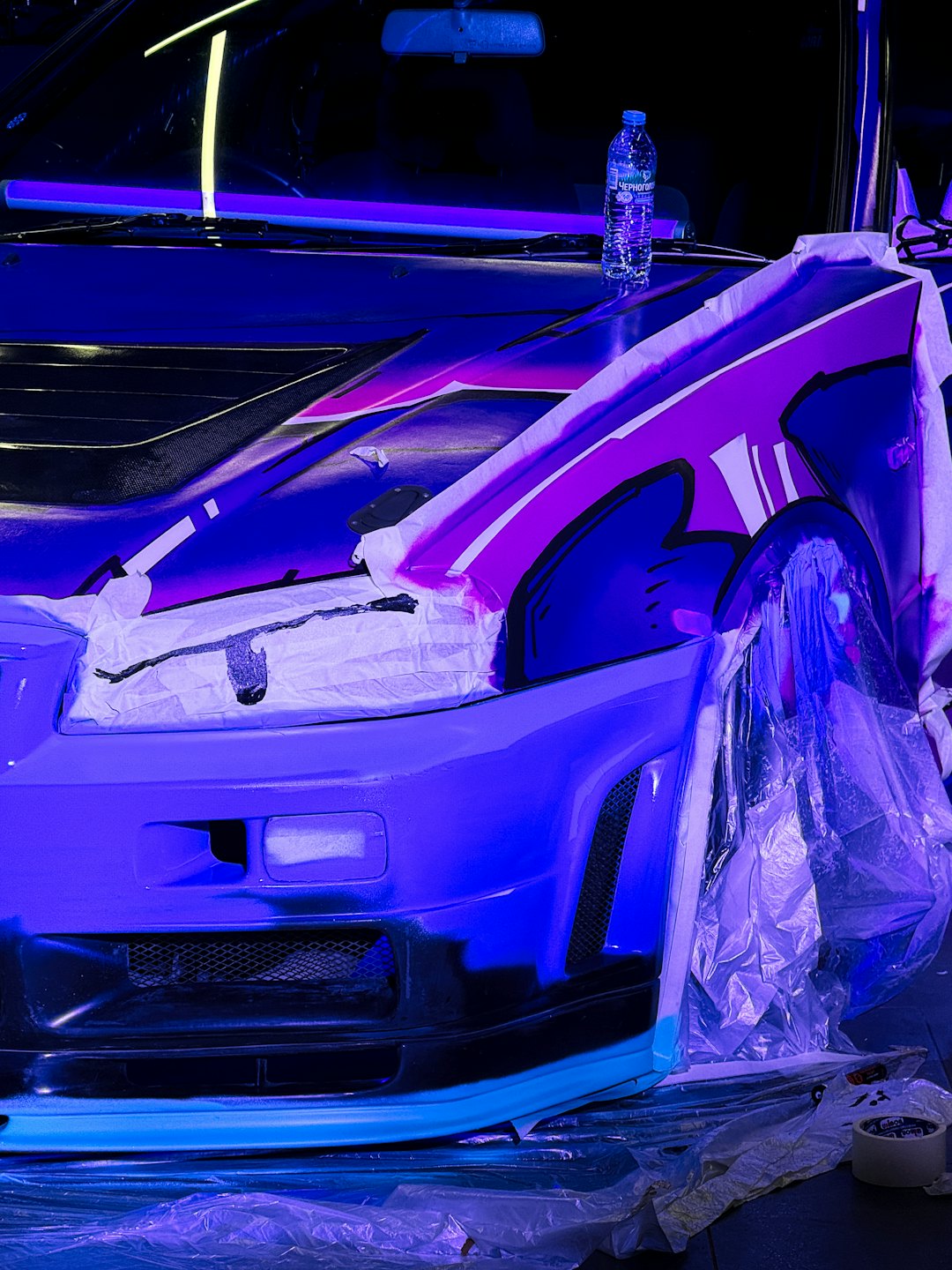 Ein Auto in einer Werkstatt wird mit Klebeband für eine individuelle Lackierung vorbereitet.